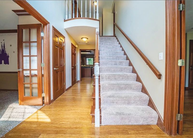 An entryway with wood floors, a carpeted staircase with a wood railing, and several wooden doors leading into other rooms.