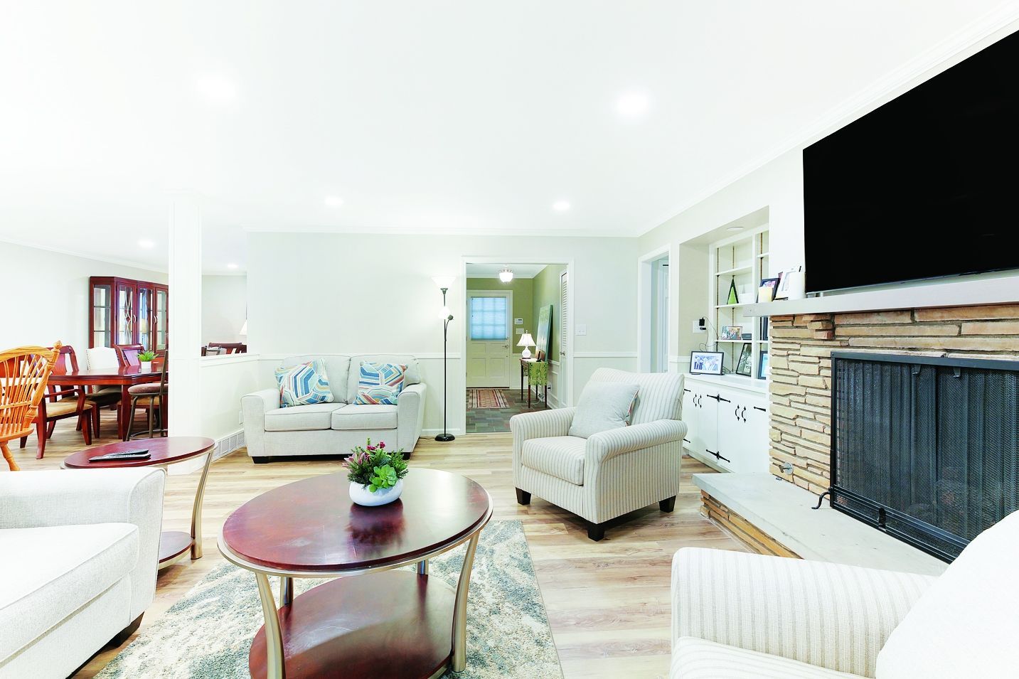 A bright, open-plan living room with a stone fireplace, cream-colored sofas, and a dark wooden coffee table.