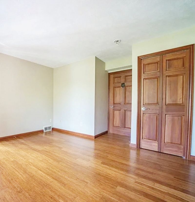 An empty room with light-colored walls, hardwood flooring, and two sets of wooden doors.