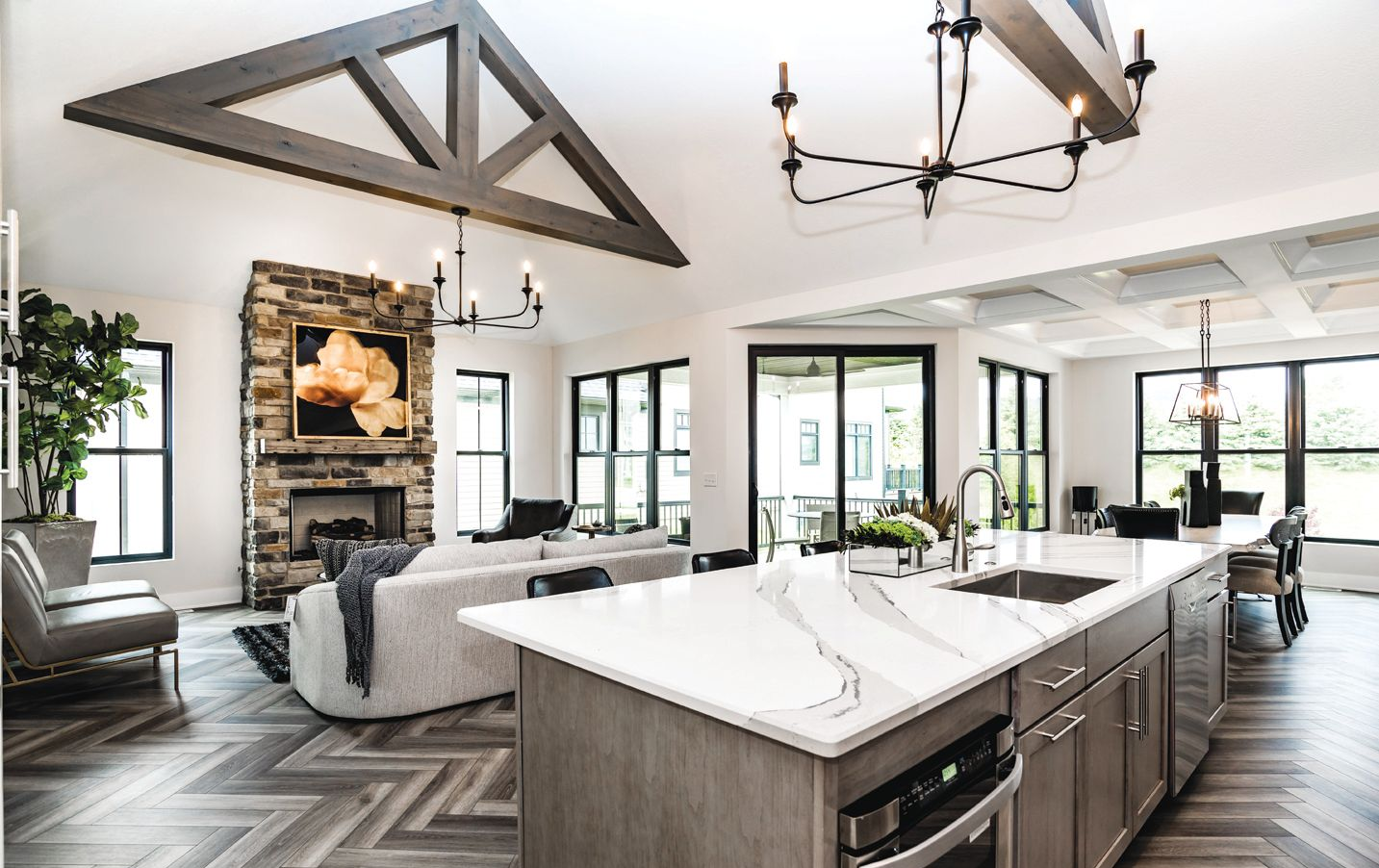 A spacious, modern open-concept living area with a stone fireplace, chevron flooring, and a large kitchen island.