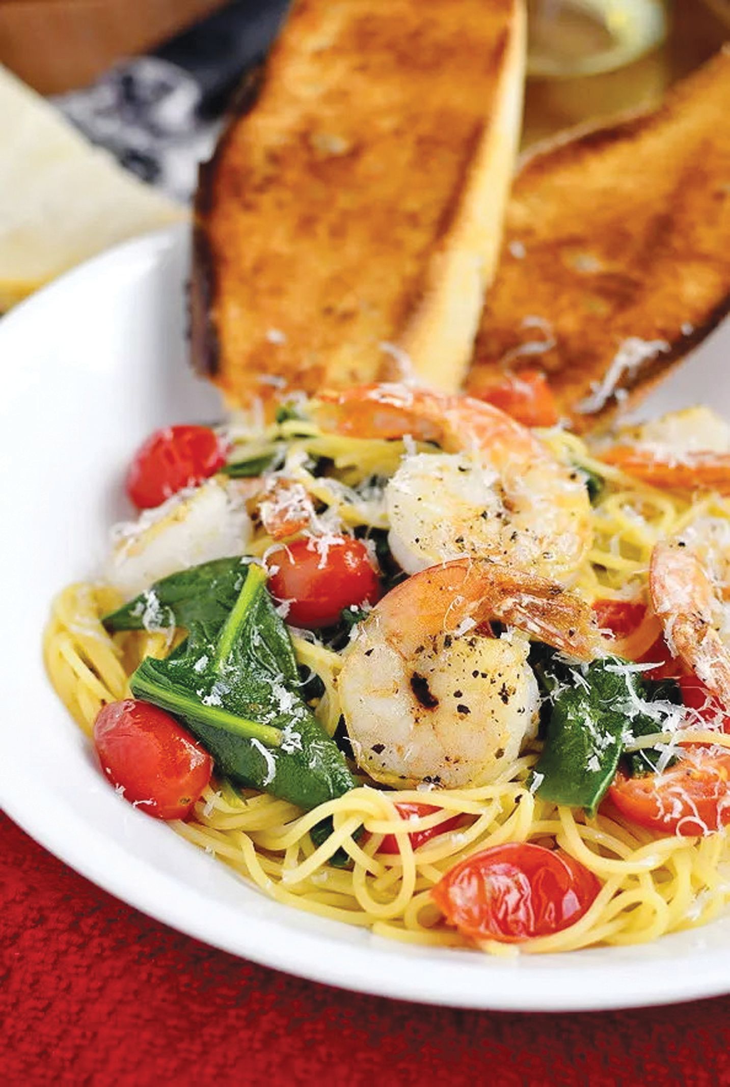 A white bowl of shrimp pasta with spinach and cherry tomatoes, topped with parmesan, served with two slices of toast.