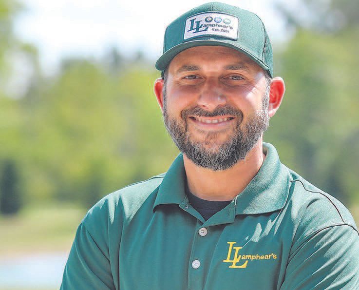 A smiling person wearing a green polo shirt and a matching baseball cap with a company logo, standing outdoors.