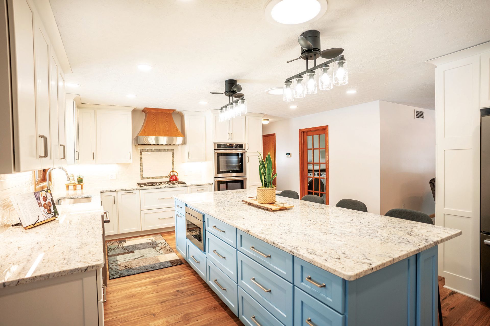 Bright kitchen with white cabinets, light blue island, granite countertops, wood floors, and a copper range hood.