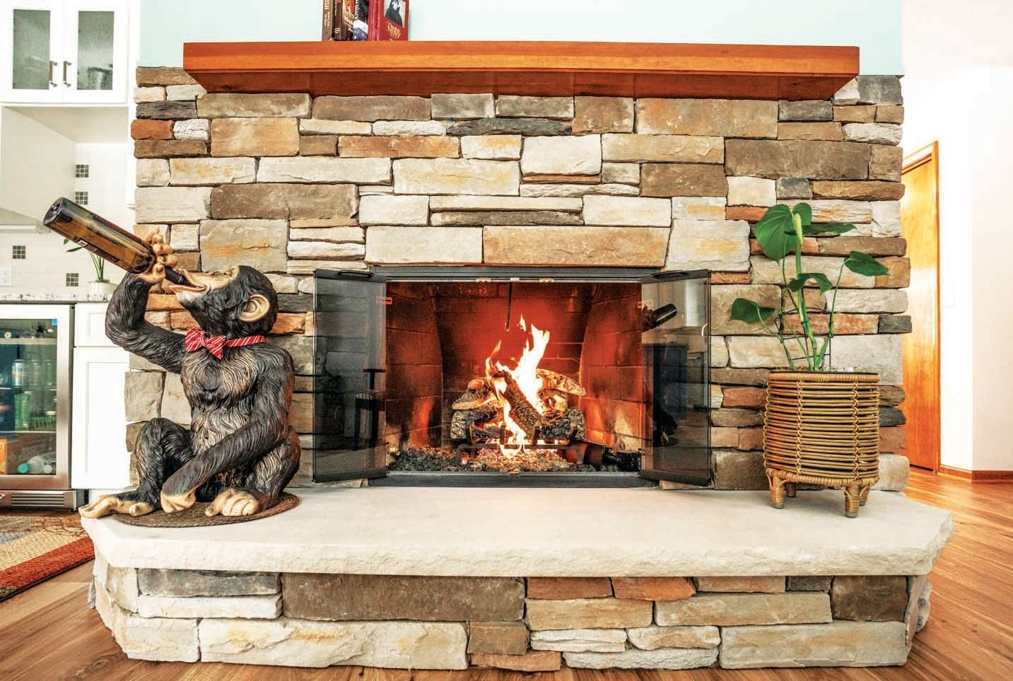 A stone fireplace with a burning fire, featuring a statue of a monkey drinking from a bottle and a small potted plant.
