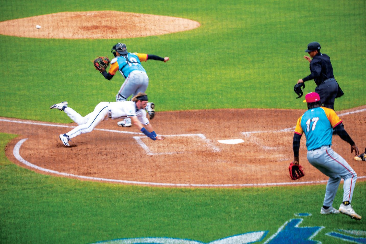 A baseball player dives headfirst toward home plate as the catcher attempts a tag, with an umpire observing nearby.