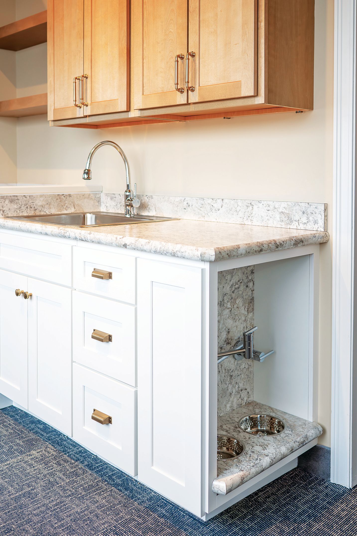 Kitchen cabinetry with a white base and wood upper cabinets, featuring a built-in pet feeding station with two bowls.
