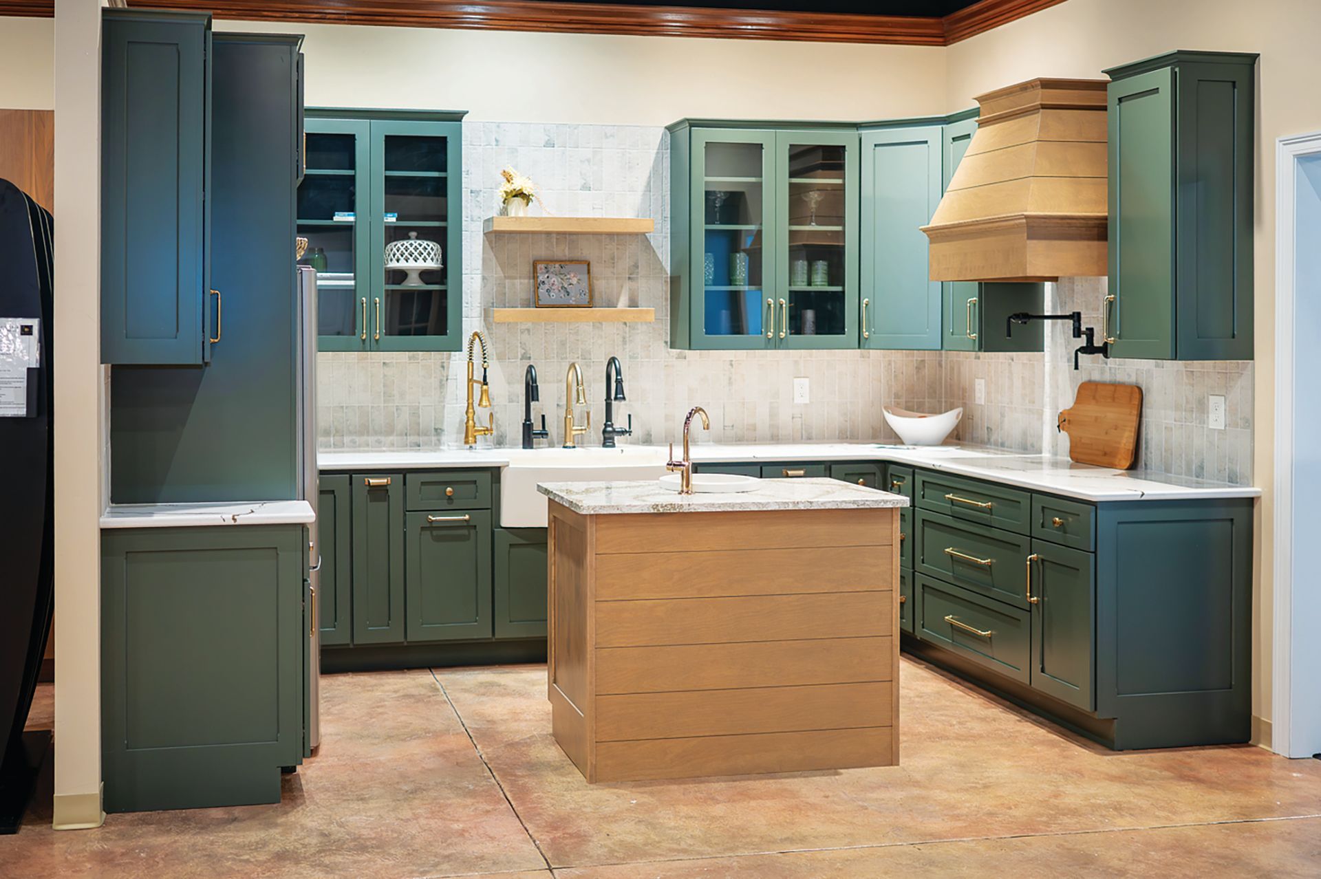 A modern kitchen featuring dark green cabinets, a light wood kitchen island, and white marble countertops.