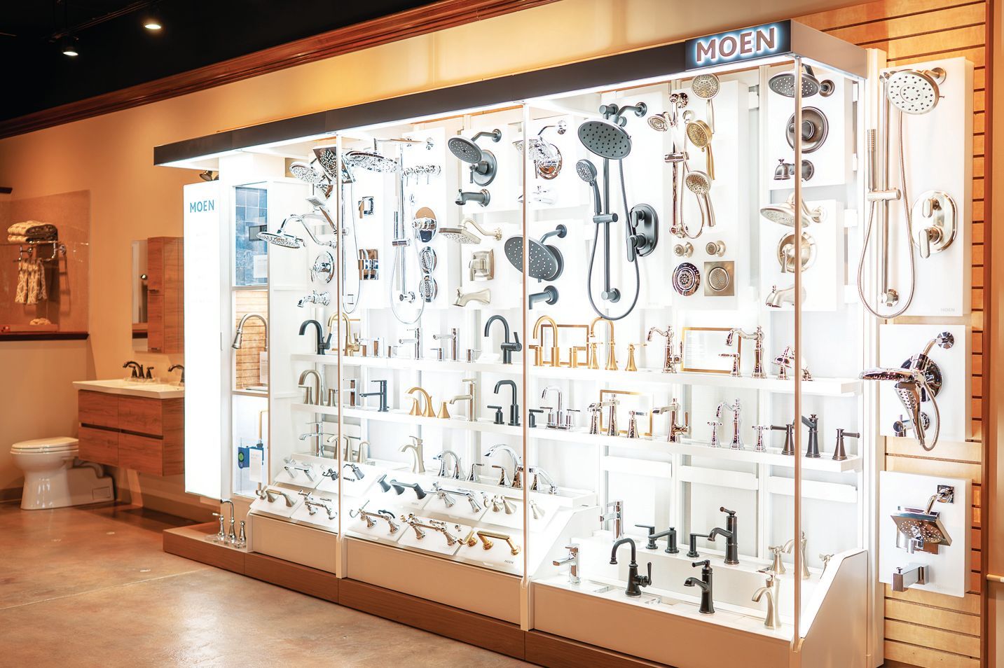 A display wall in a showroom featuring various Moen bathroom faucets and shower fixtures, organized on lit shelves.