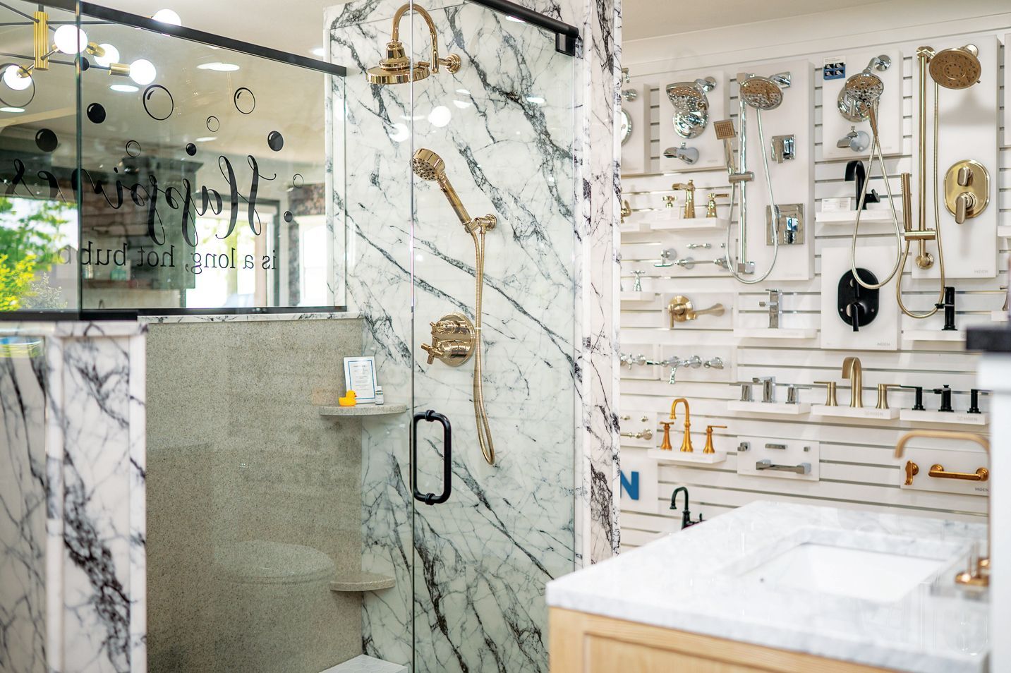 A bathroom showroom display featuring a marble-tiled shower stall and walls filled with mounted gold plumbing fixtures.