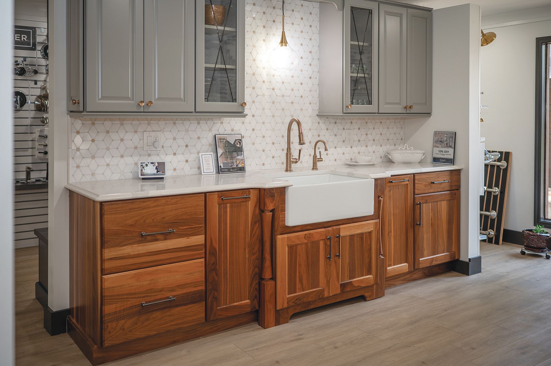 A kitchen vignette featuring gray upper cabinets, natural wood lower cabinets, a farmhouse sink, and white hex backsplash.