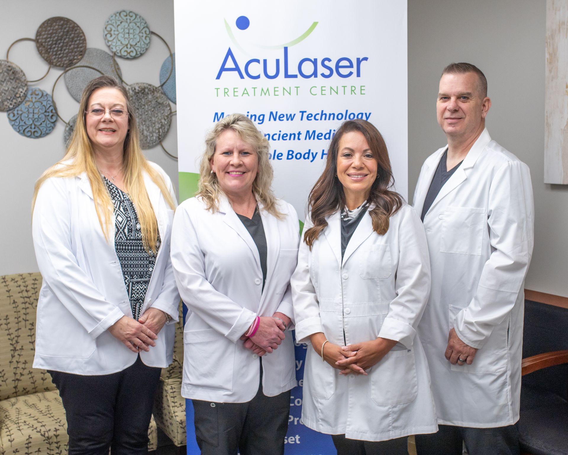 Four staff members in white lab coats stand in front of an AcuLaser Treatment Centre sign in a professional office.