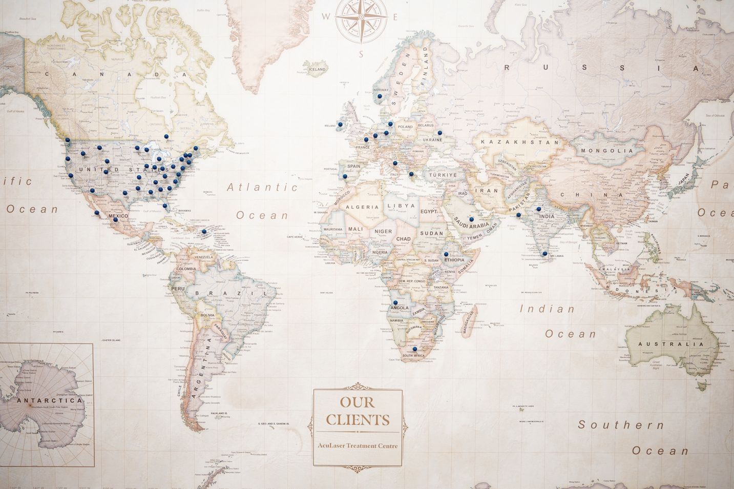A vintage-style world map featuring blue pins placed across North America, Europe, and parts of Asia, Africa, and Australia.