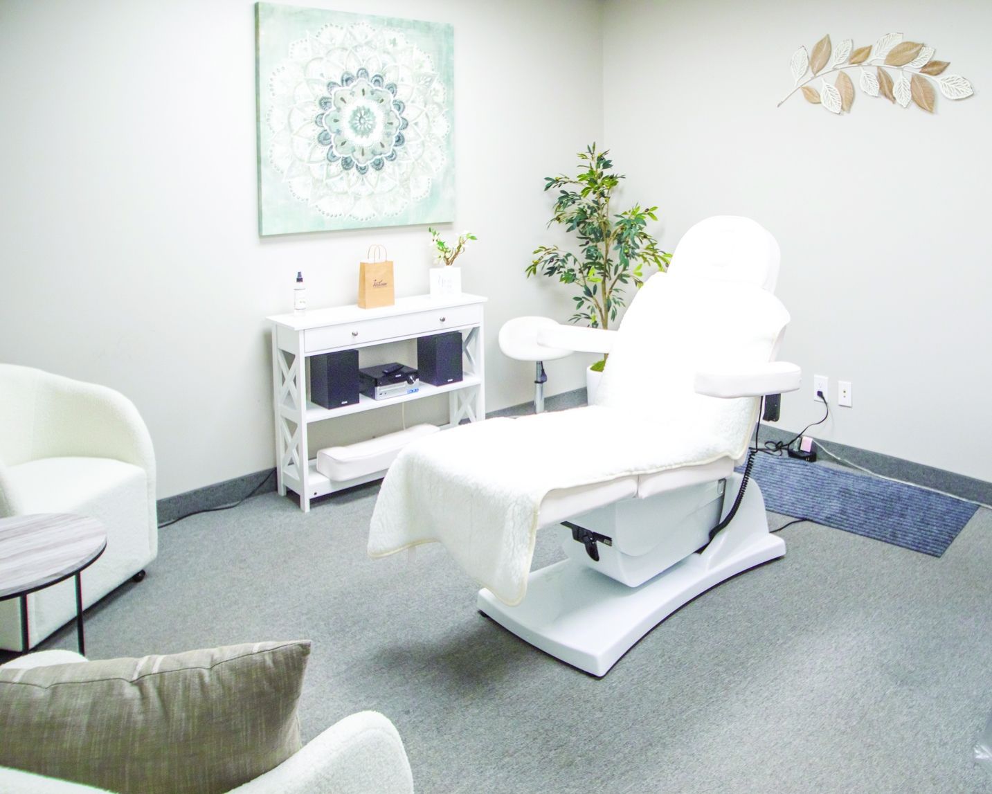 A clean aesthetic treatment room with a white reclining procedure chair, a white side table, and minimalist wall decor.