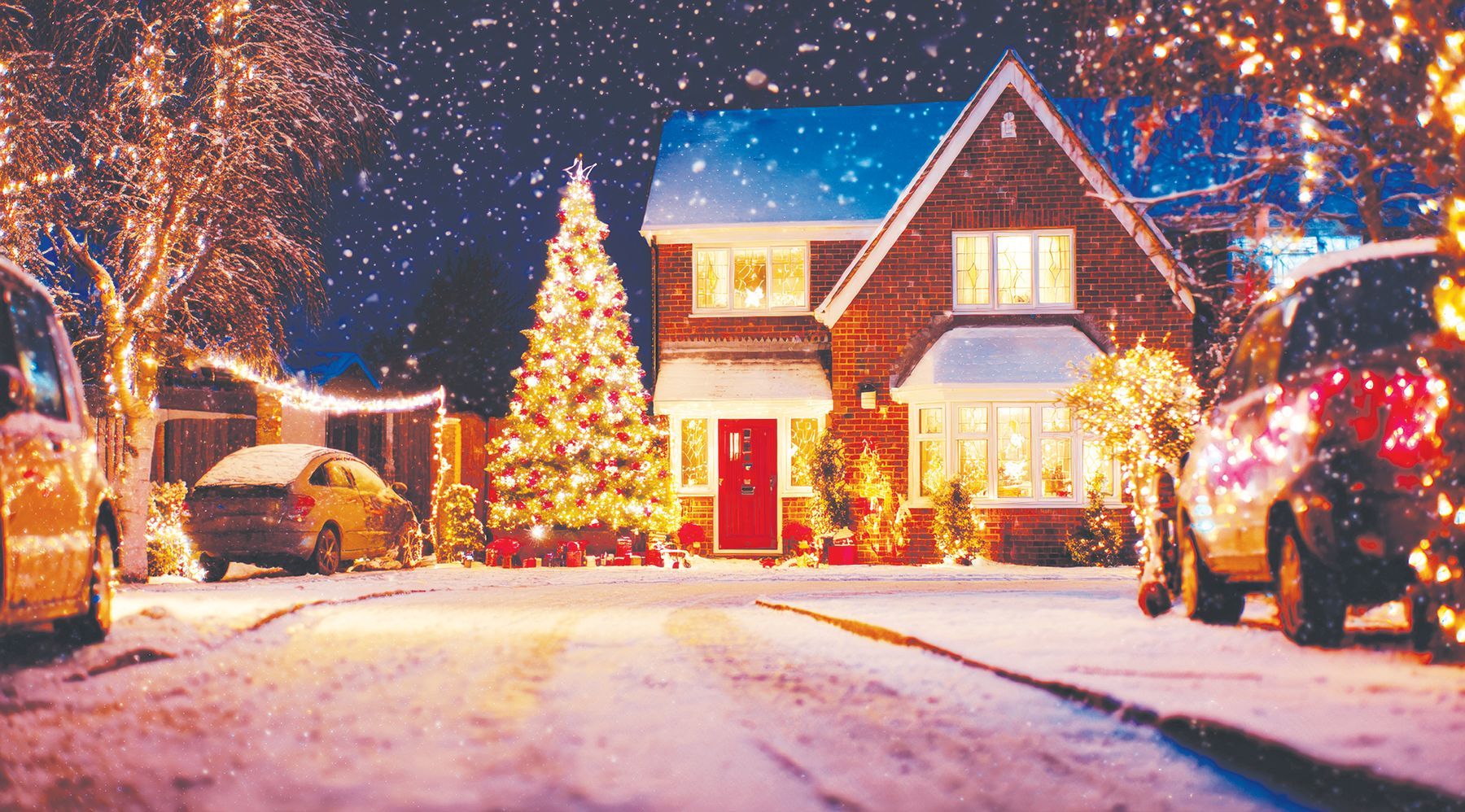 A cozy suburban home decorated with warm Christmas lights and a large, glowing tree in the yard during a snowy night.
