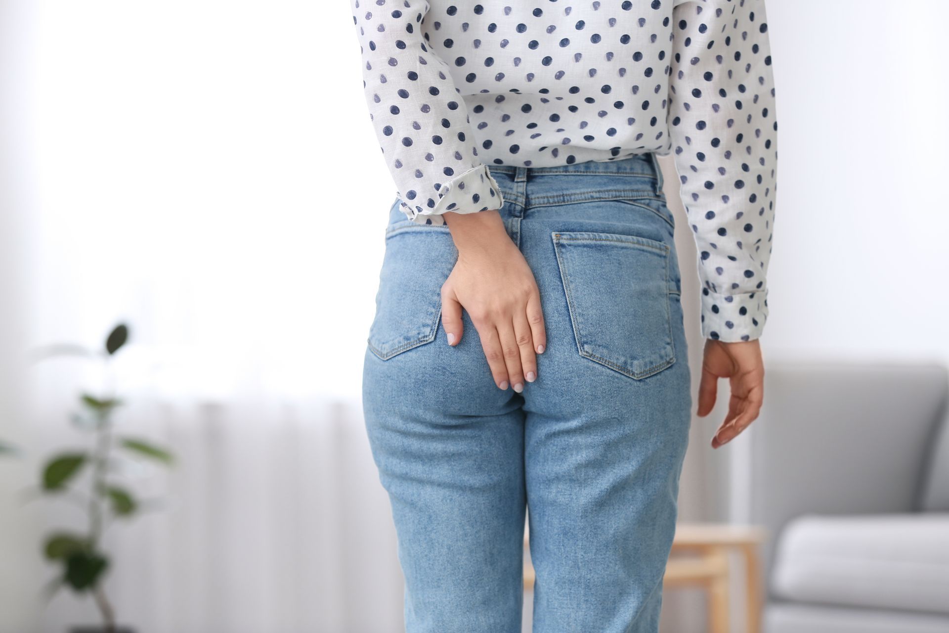A person in a polka-dot shirt and blue jeans reaches back to touch their hip, suggesting discomfort or pain.