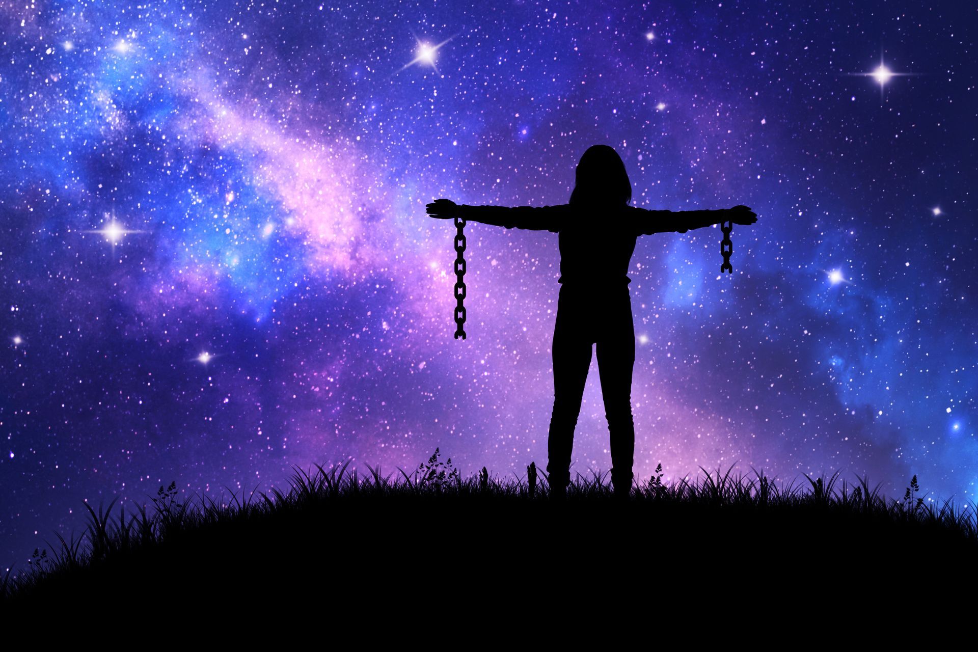 A silhouette of a person standing on a grassy hill with arms outstretched, holding broken chains against a starry sky.
