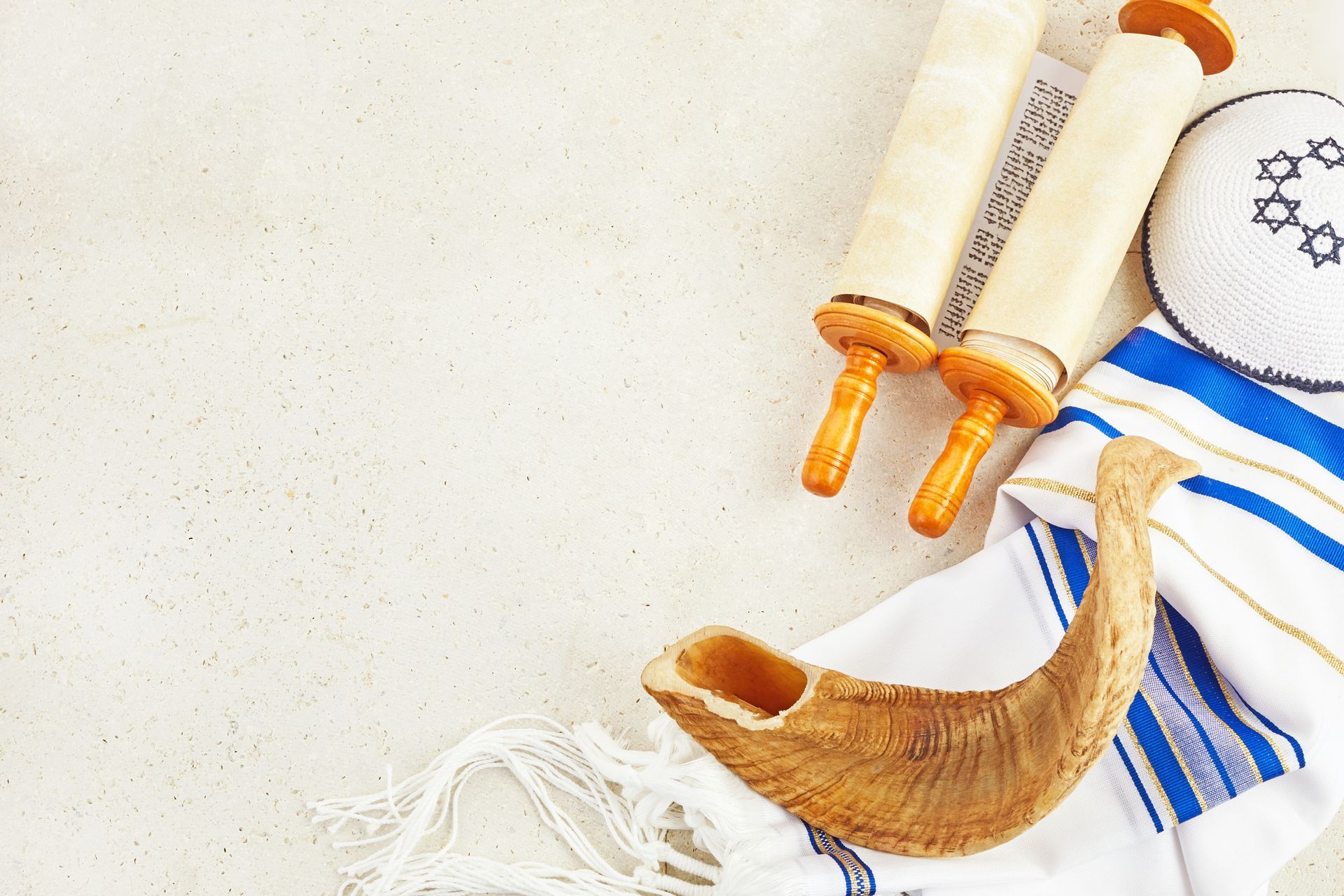 A Torah scroll, a shofar, a tallit prayer shawl, and a kippah arranged on a light background.