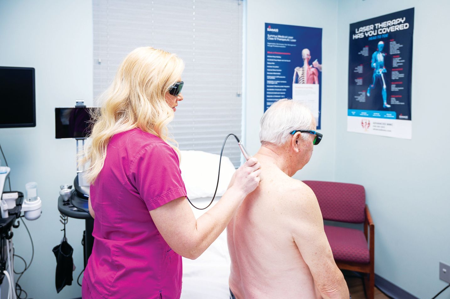 A practitioner uses a handheld laser device on a patient’s back in a clinical office setting.