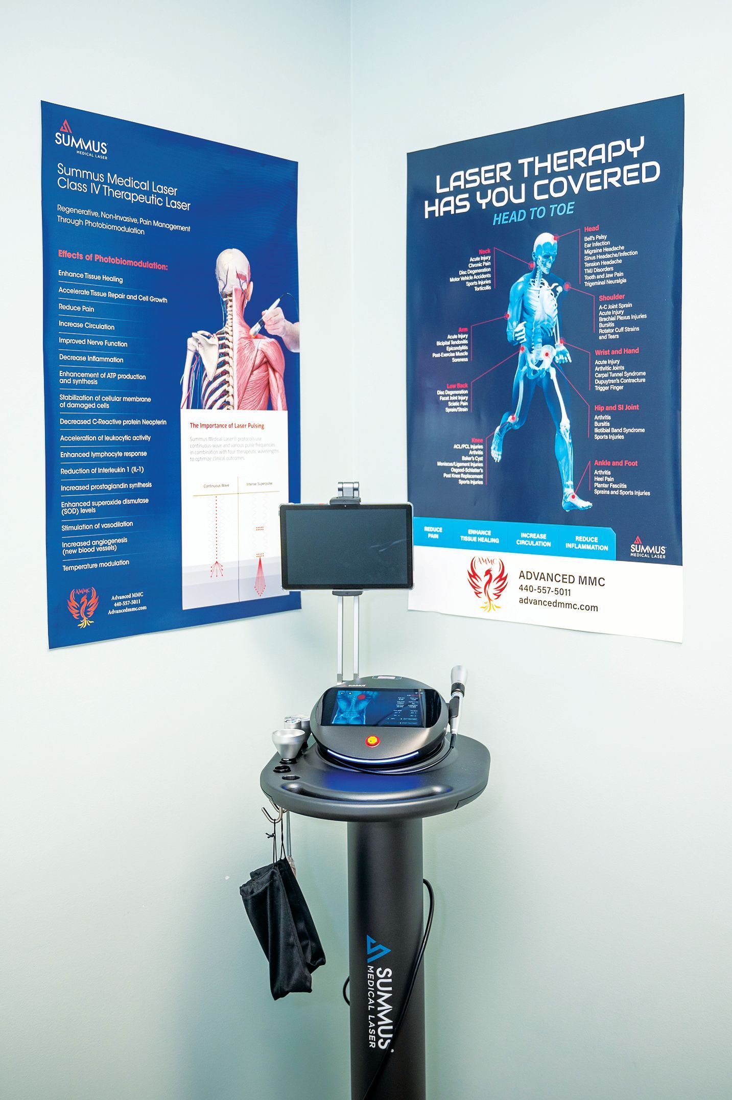 A laser therapy machine stands in a corner between two informational posters on a light-colored wall.
