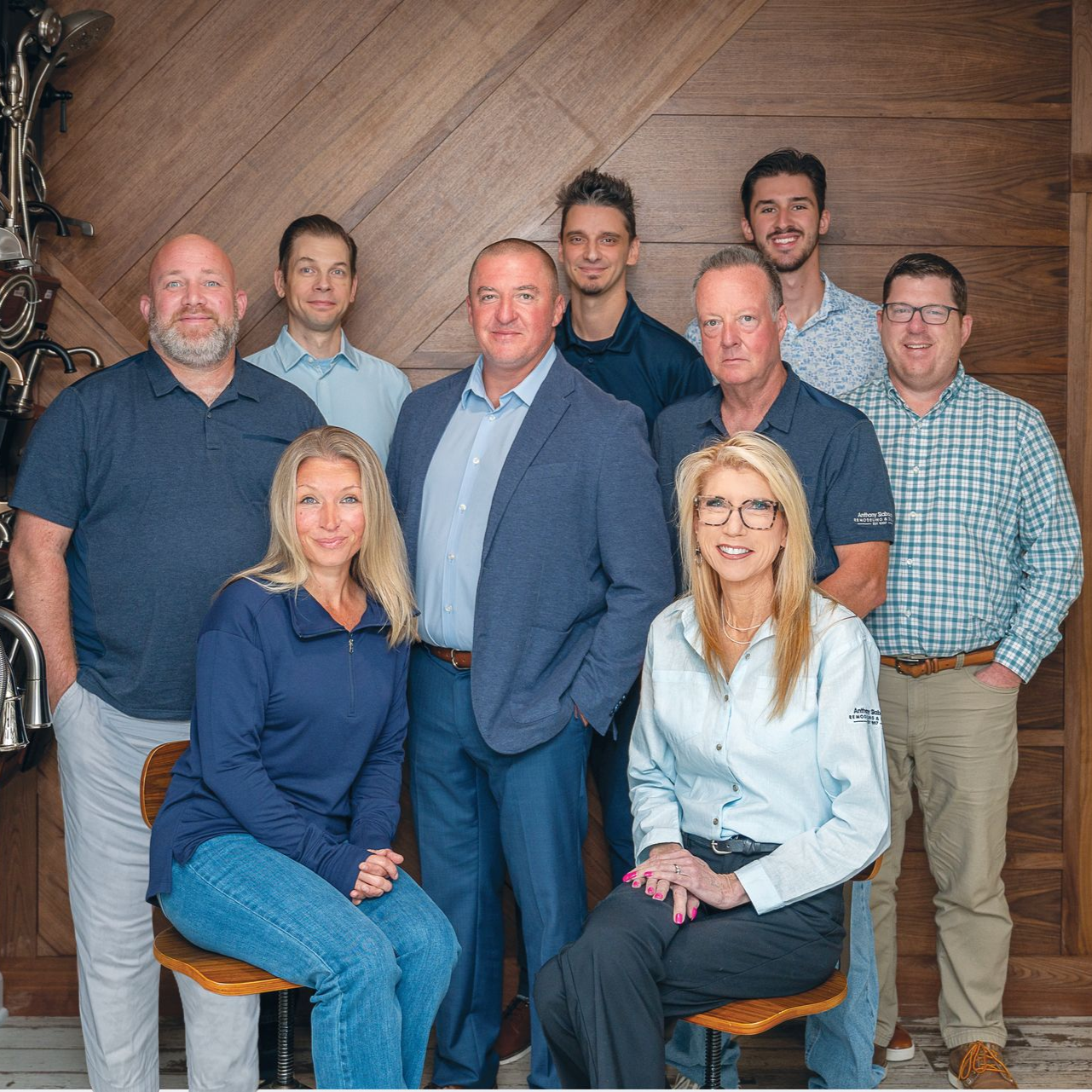 A group of ten colleagues posing for a team photo in front of a wood-paneled wall, all dressed in business casual attire.