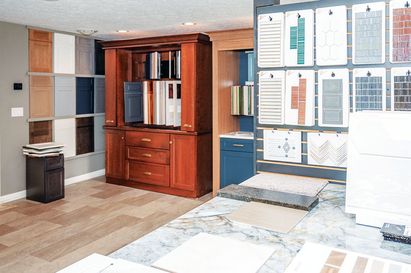 A design showroom featuring wood cabinetry, display racks with material samples, and a stone-topped island.