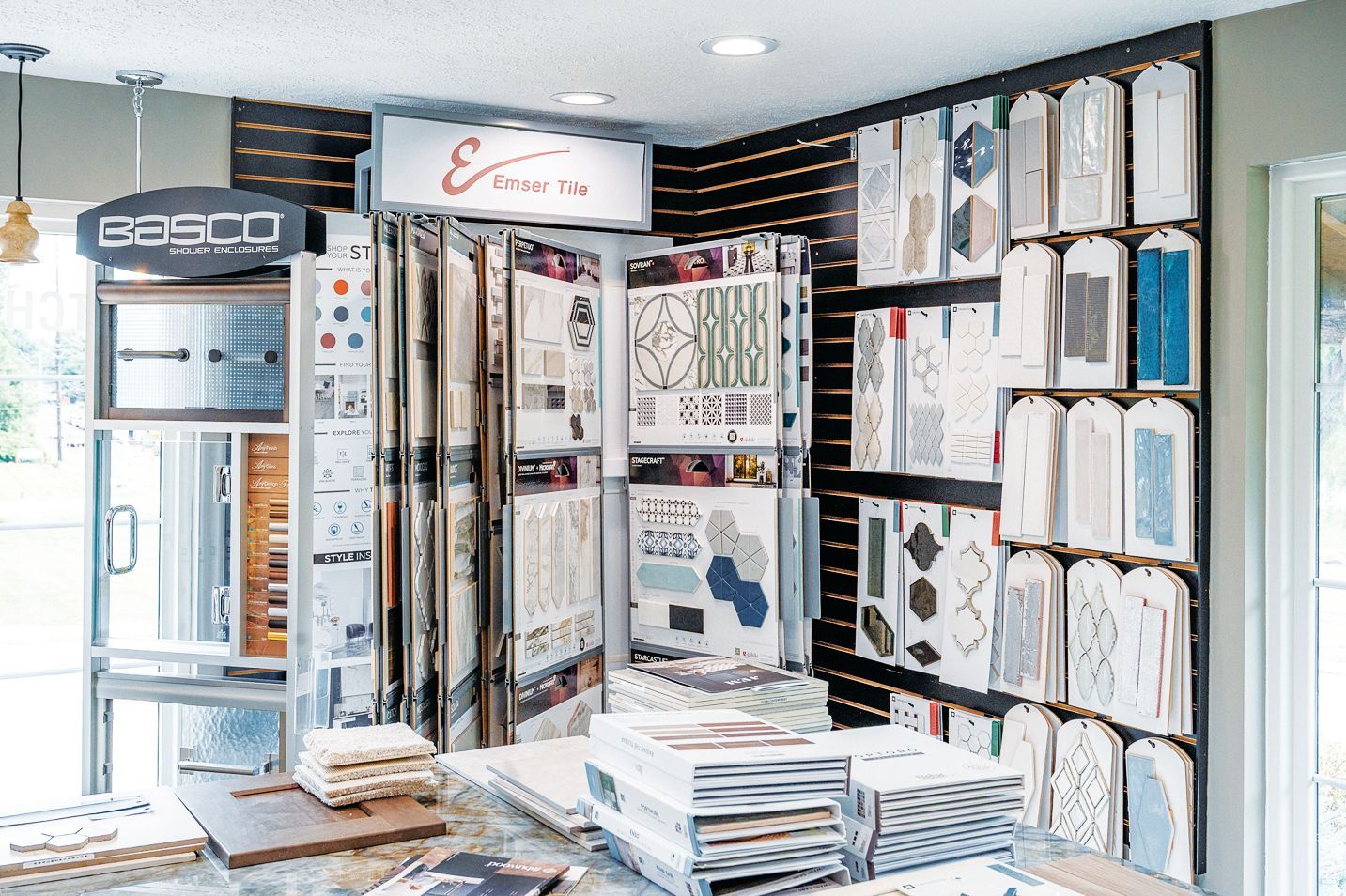 A showroom featuring display racks, binders, and wall-mounted samples of various tile, fabric, and design materials.