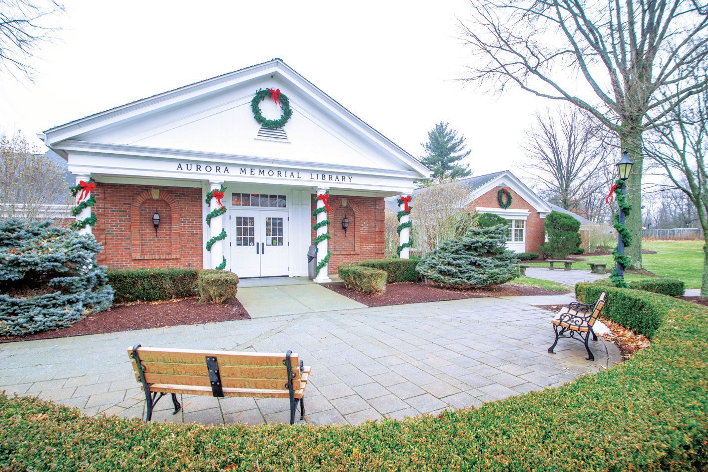 Brick building with a pediment, wreath, and holiday decorations, featuring a stone courtyard with two wooden benches.