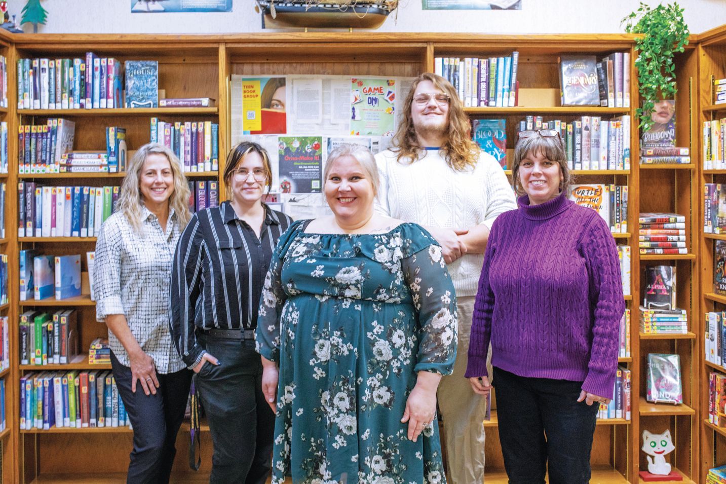Five people stand smiling in front of a library bookshelf filled with colorful books.