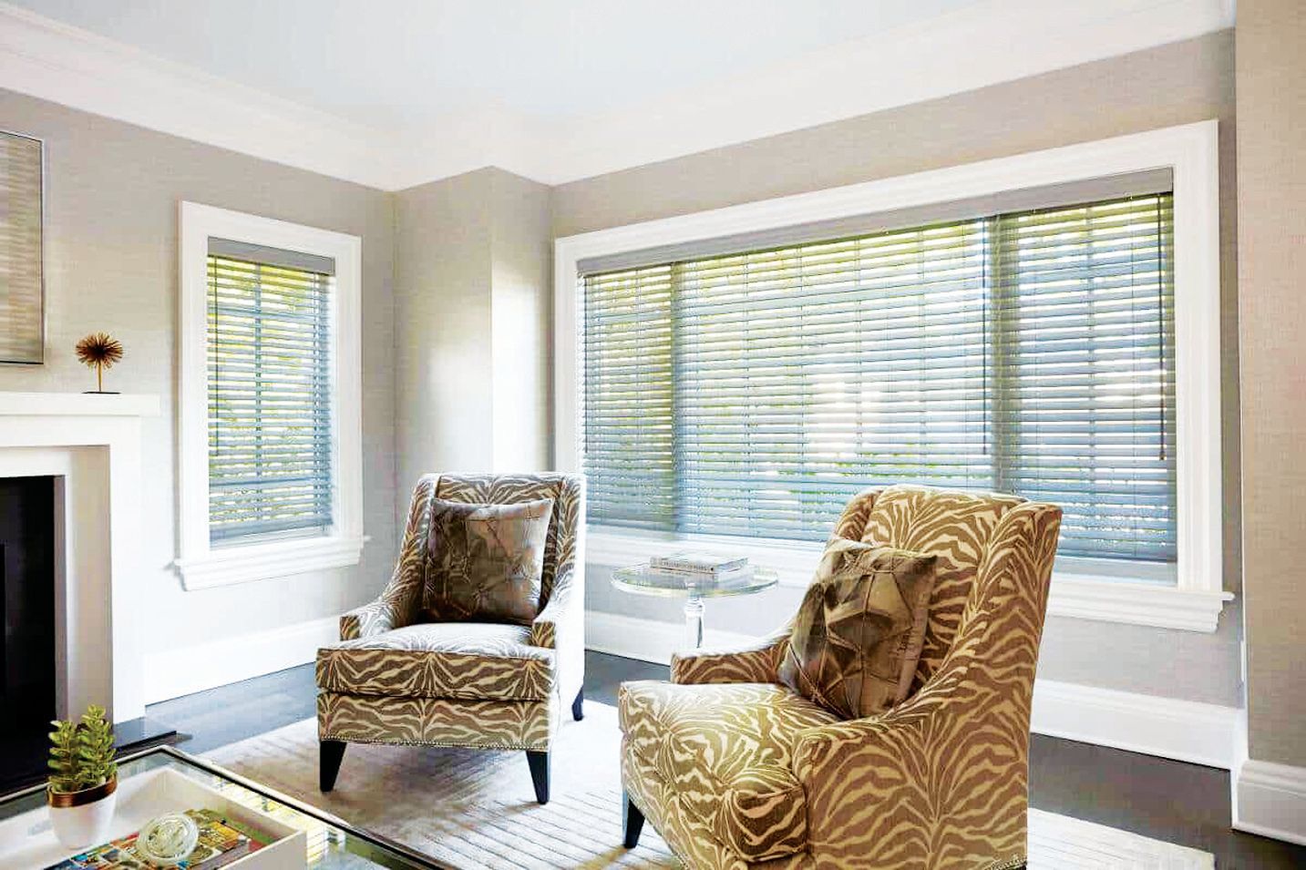 Two patterned armchairs sit in a bright, modern room near a fireplace and large windows with horizontal blinds.