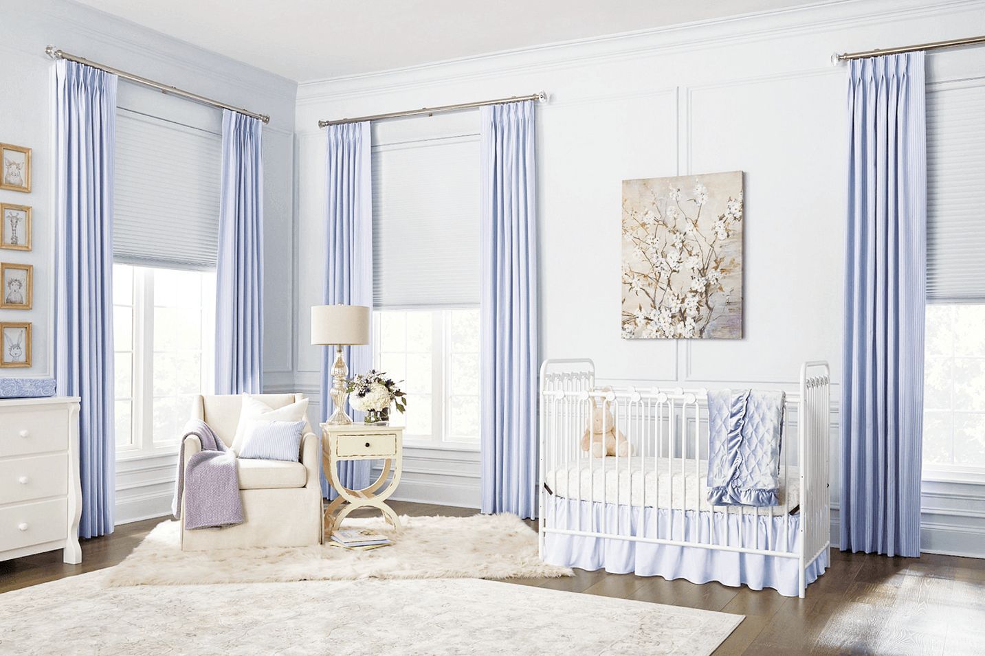 A bright, blue and white nursery featuring a white crib, an armchair with a throw blanket, and blue curtains over windows.