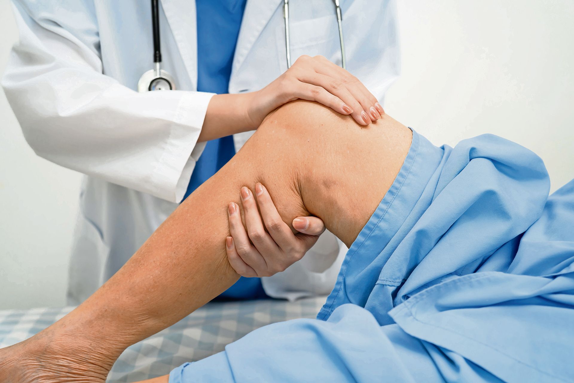 A healthcare professional in a white coat performs a physical examination of a patient's knee.