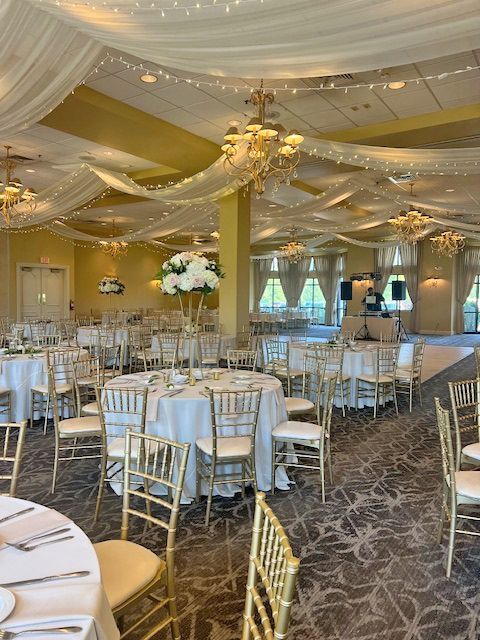 A banquet hall set for a wedding reception with round tables, gold chairs, white tablecloths, and floral centerpieces.