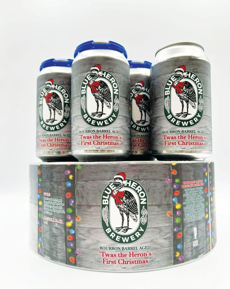 Four Blue Heron Brewery beer cans featuring a Christmas-themed label and an unrolled matching adhesive roll.