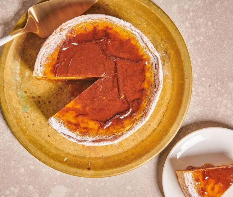 A round flan with a glossy, caramelized top sits on a gold plate, with a slice served on a small white side plate.
