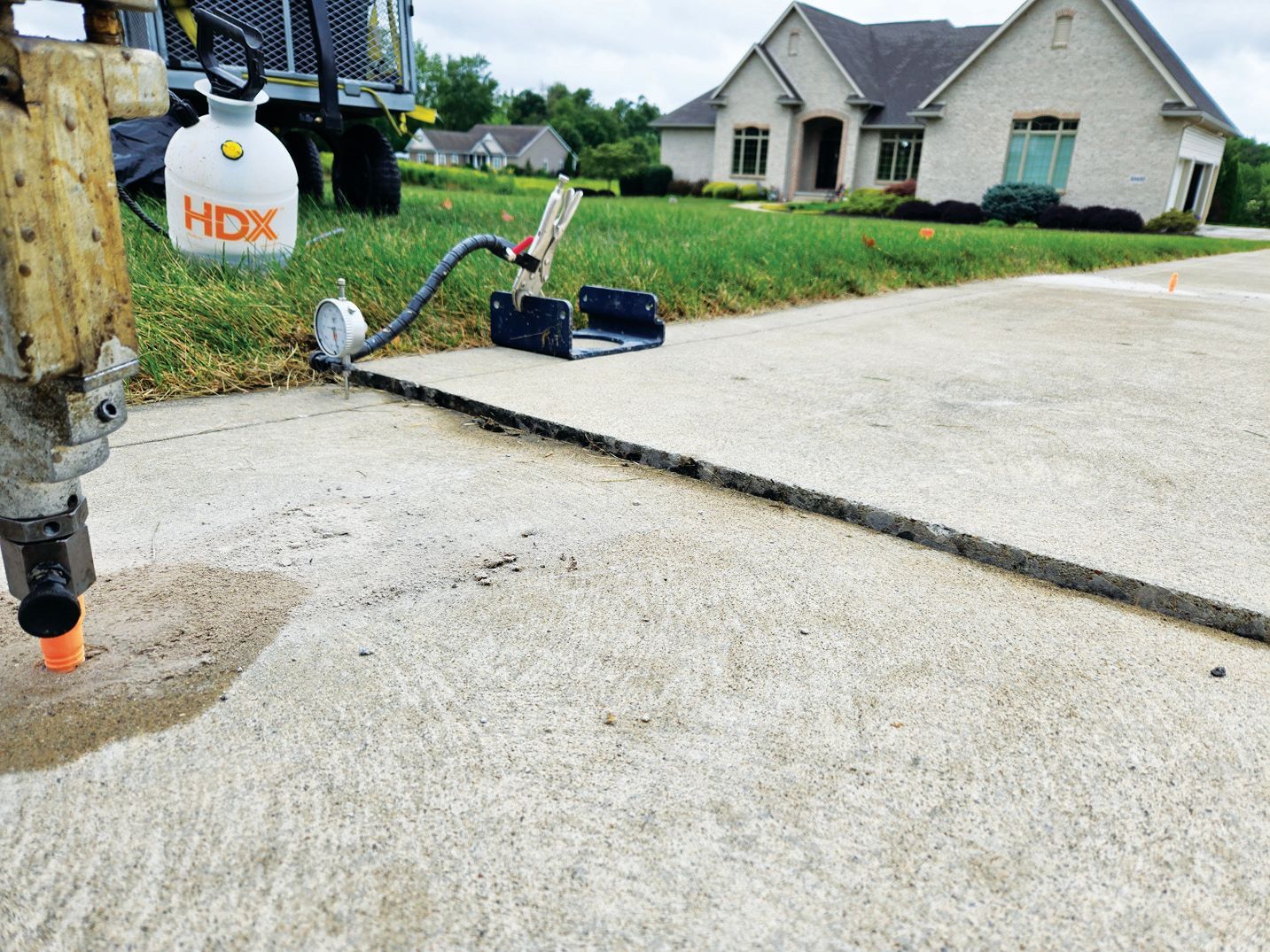 Concrete leveling equipment injecting foam into a slab joint near a residential house.