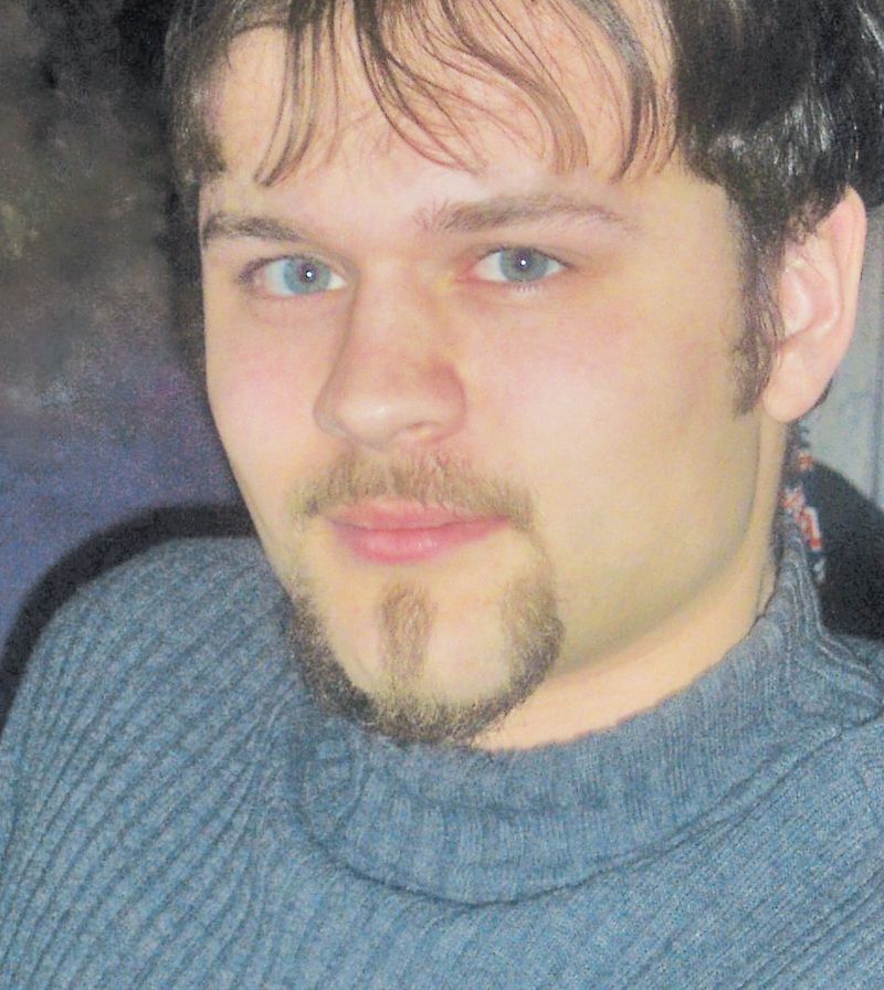 A headshot of a person with blue eyes and a goatee, wearing a grey sweater, looking toward the camera.