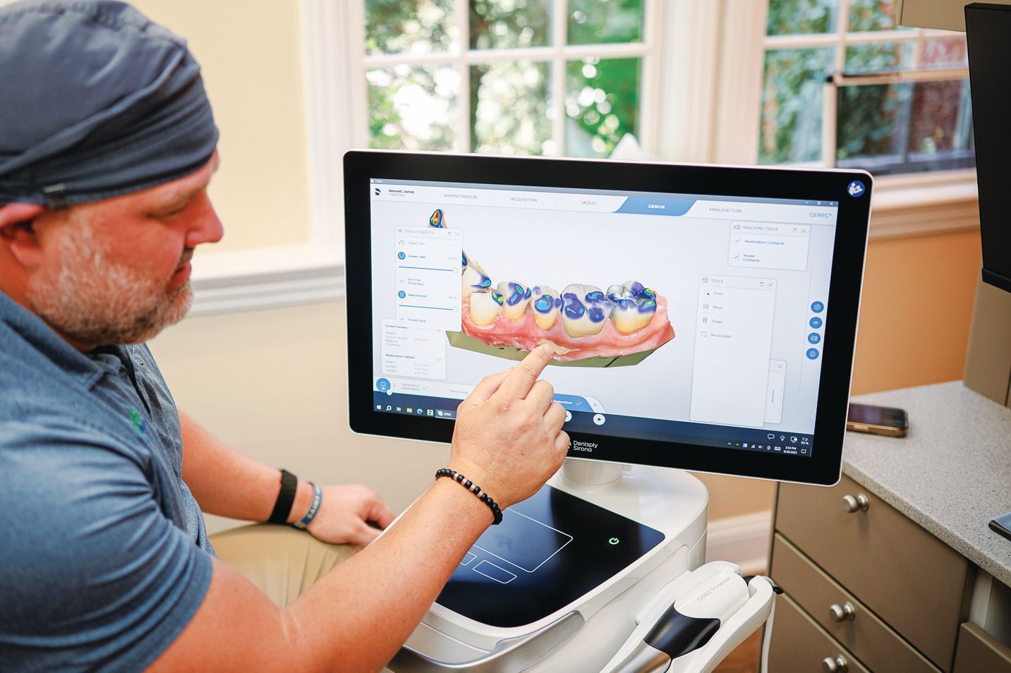 A person points to a 3D dental scan of teeth and gums displayed on a computer screen in a professional office.