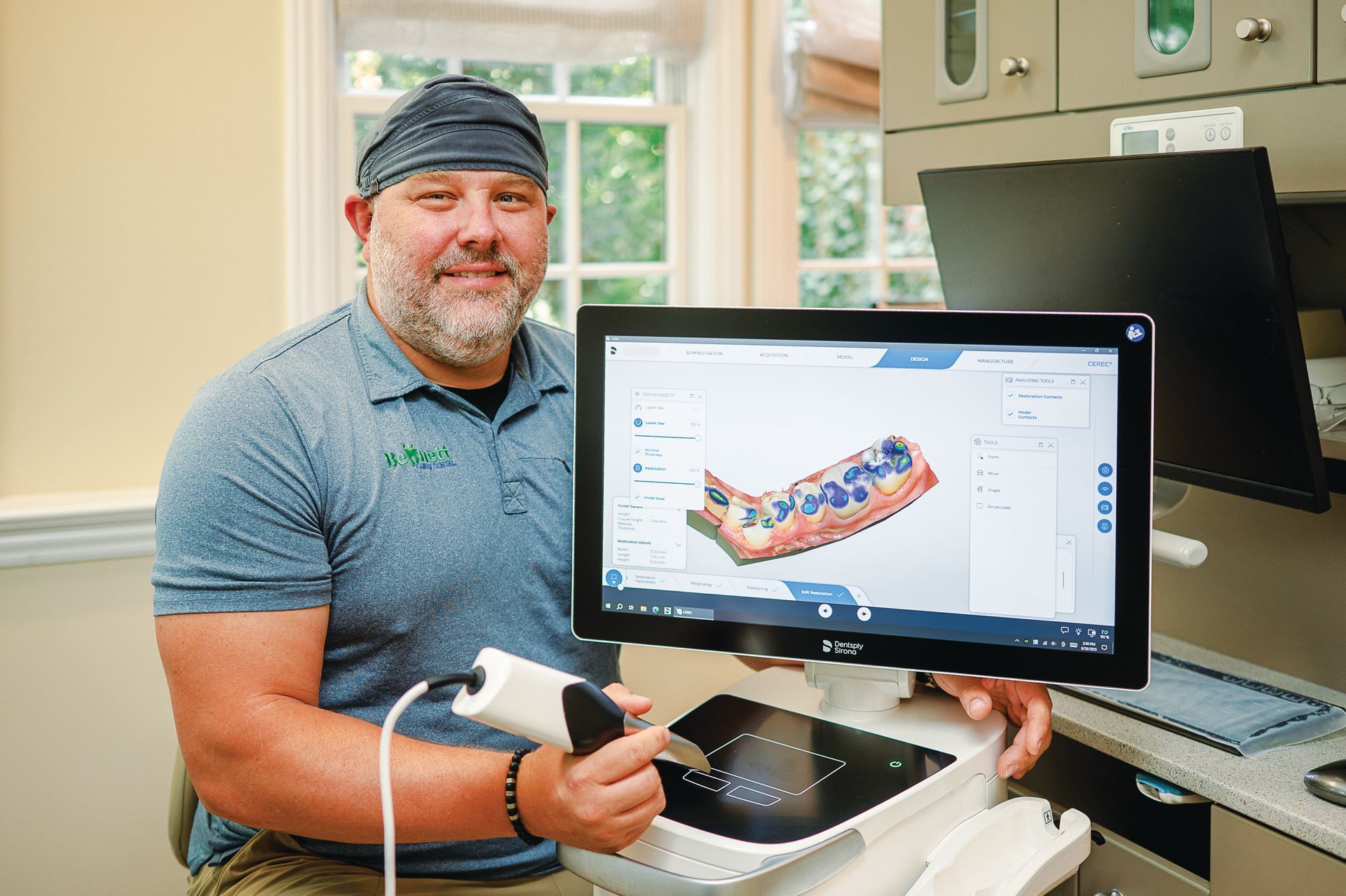 A person in a dental office holds a digital scanner next to a monitor displaying a 3D dental impression.