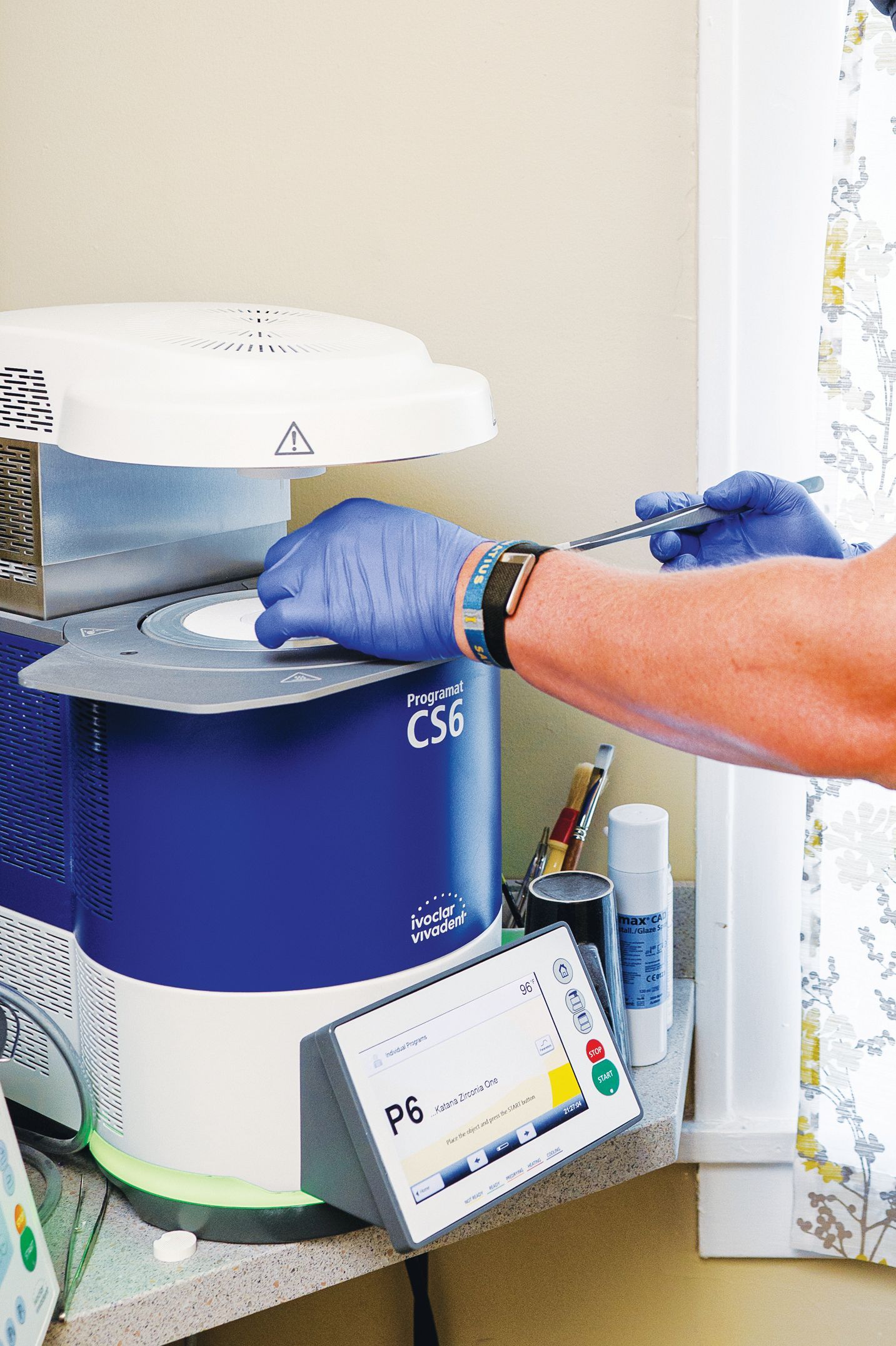 A person wearing blue gloves places a sample into a blue and white C56 laboratory centrifuge.