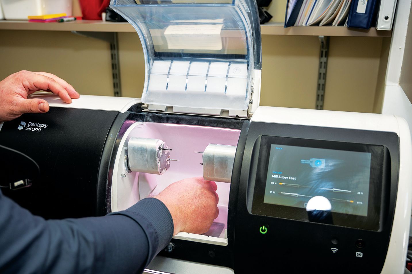 A person inserts a small dental prosthetic block into a dental milling machine in a lab setting.