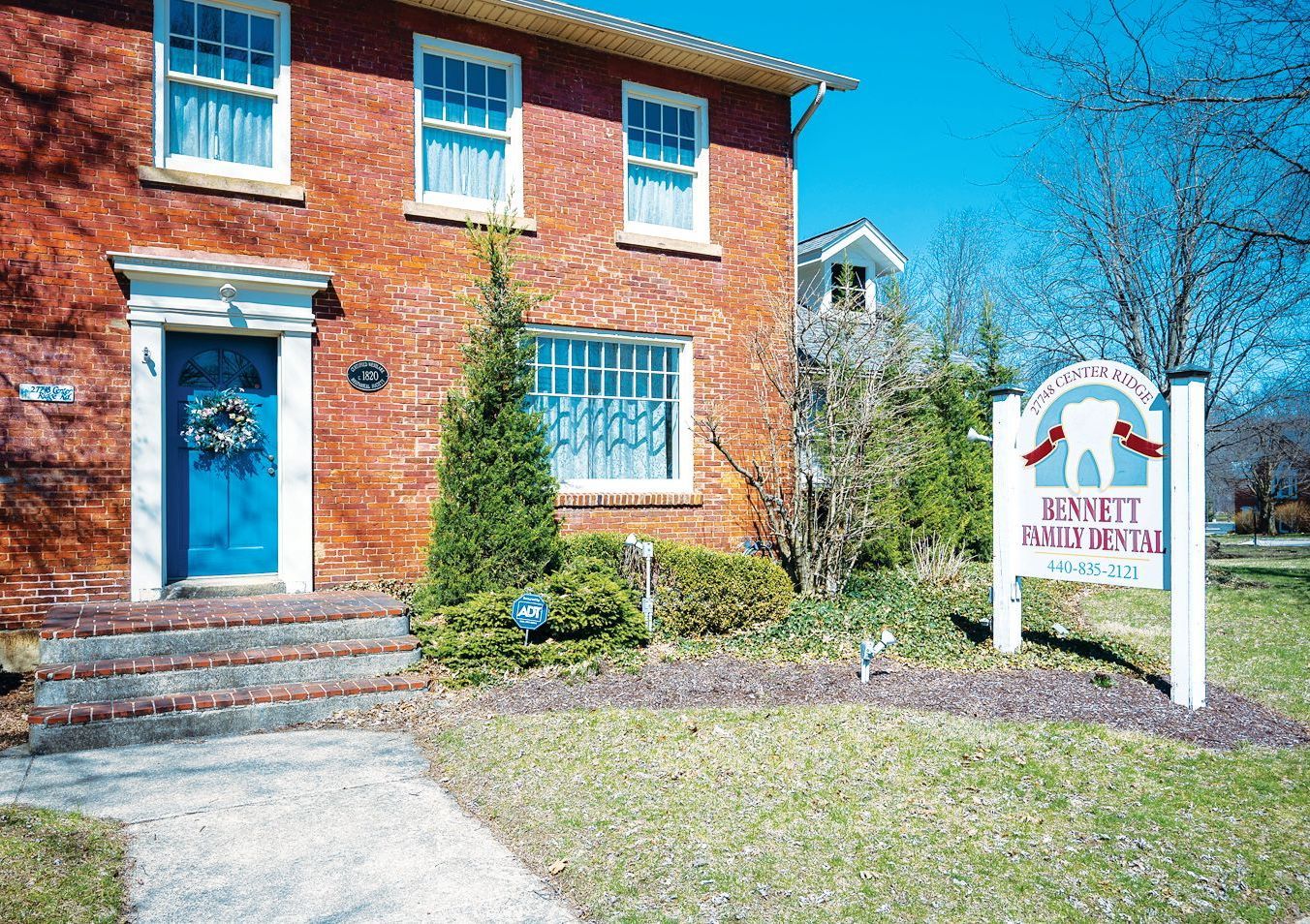 A red brick building with a blue front door and a sign for Bennett Family Dental in the front yard.