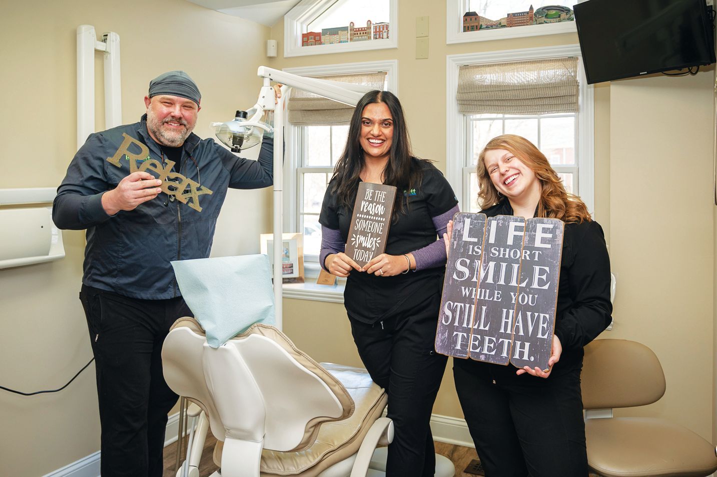 Three smiling people in a dental office hold signs that read 