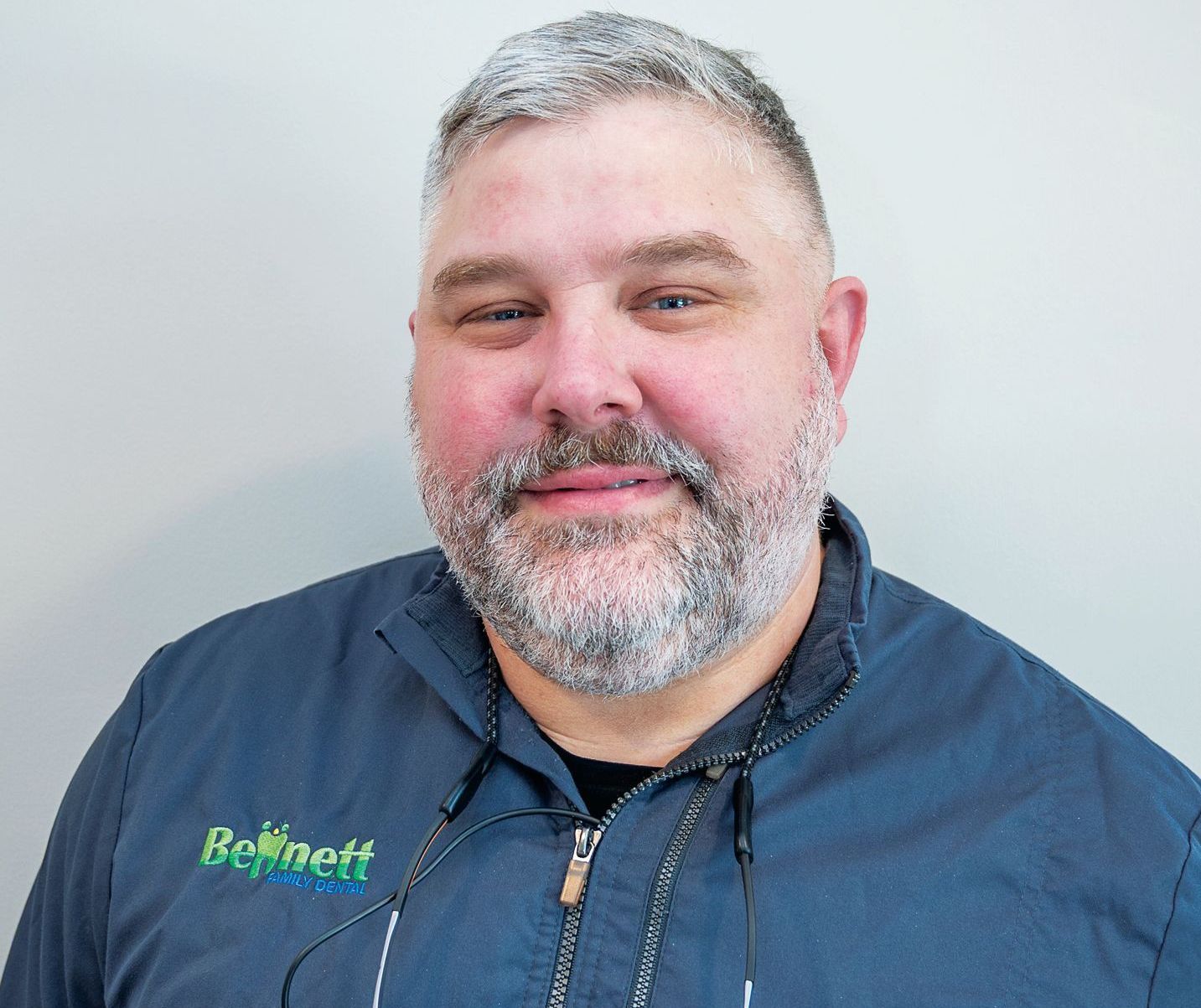 A person with a beard and graying hair, wearing a dark blue zip-up shirt with a green 
