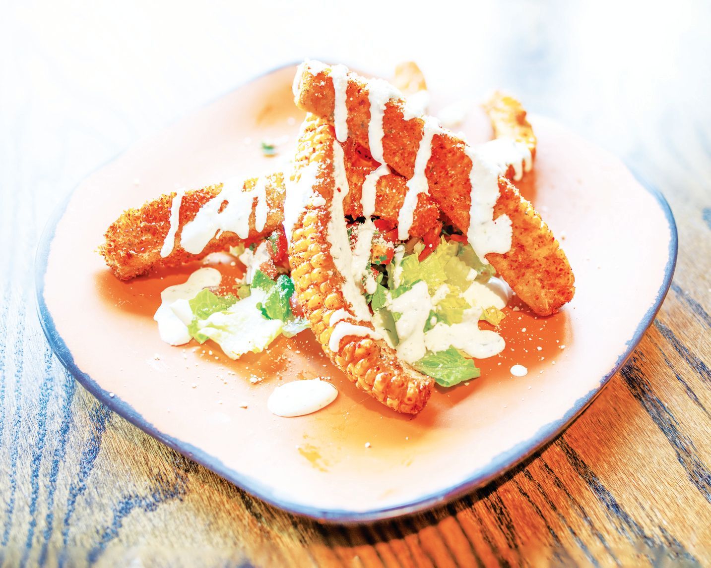 A serving of fried breaded appetizers drizzled with white sauce and garnished with green herbs on a light-colored plate.