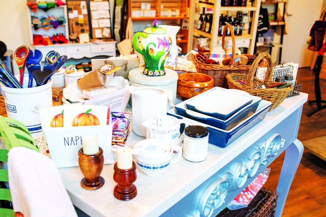 A shop table displays a variety of home decor, including kitchenware, candles, baskets, and festive napkins.