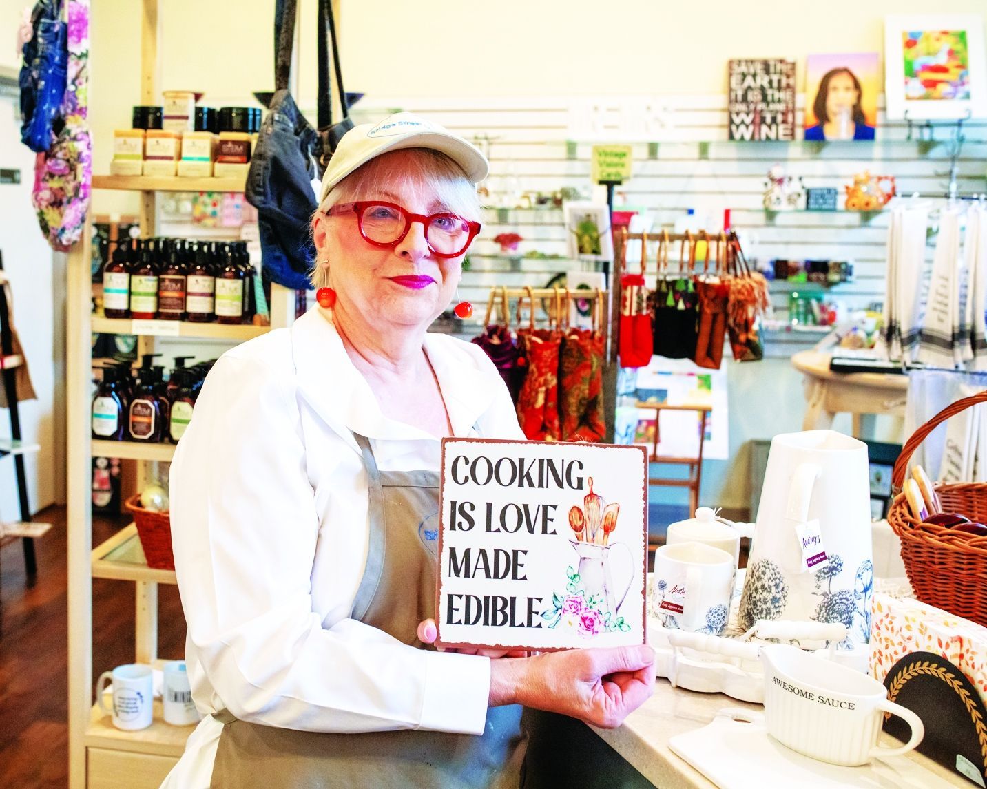 A person wearing a hat and apron holds a small square sign reading 