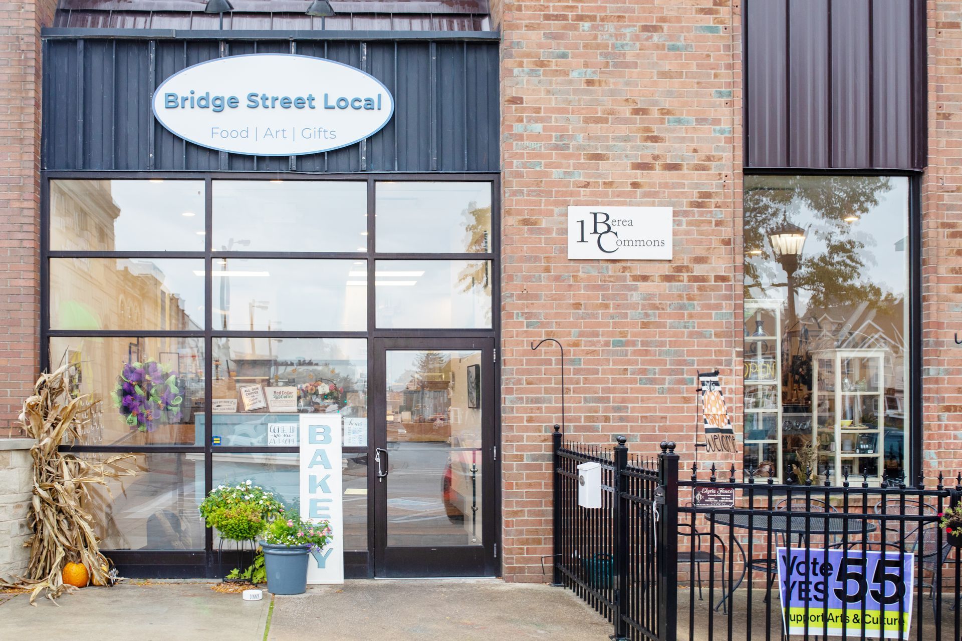 The storefront of Bridge Street Local bakery, featuring a large glass window, brick facade, and a small patio area.