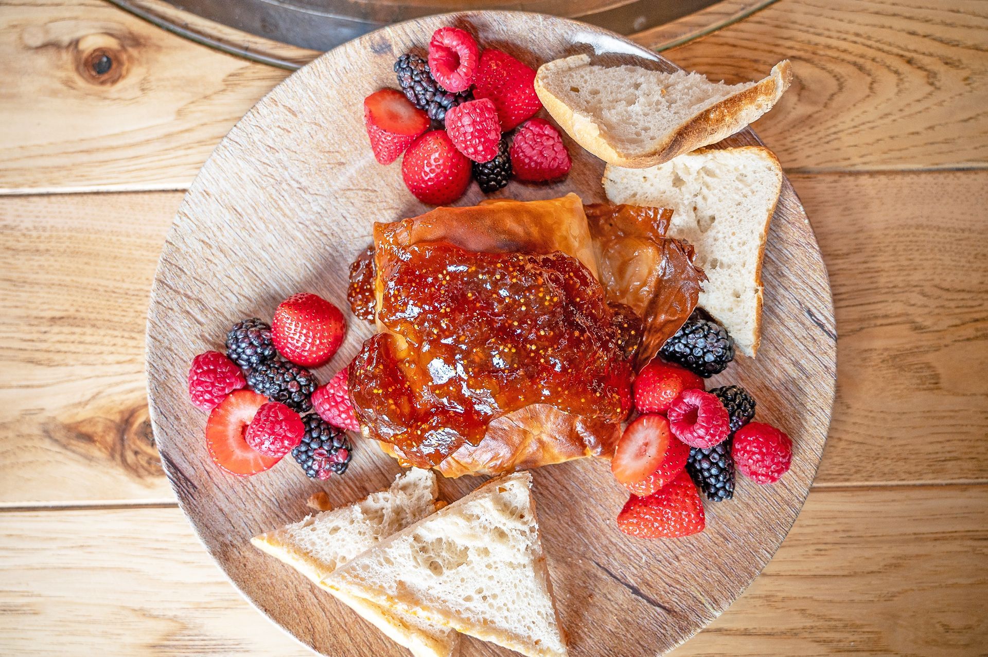 A plate of French toast topped with berry jam, served with fresh raspberries, blackberries, strawberries, and bread.