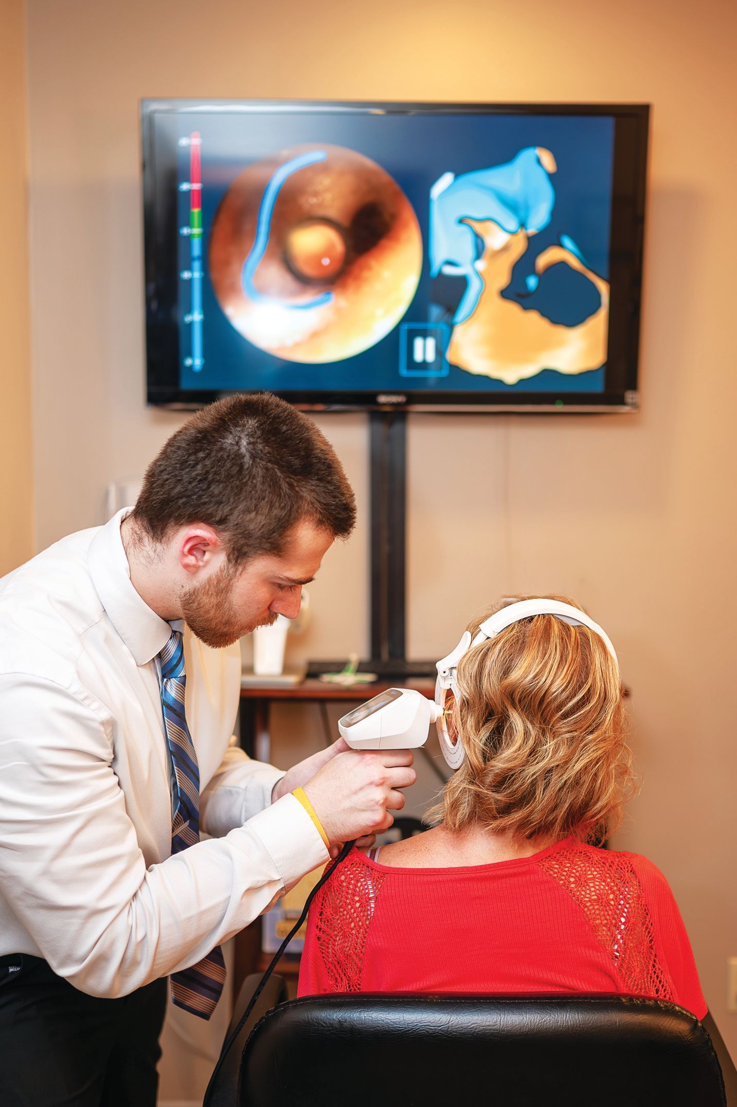 A professional uses a digital tool to examine a patient’s ear, with the inner ear view displayed on a nearby monitor.