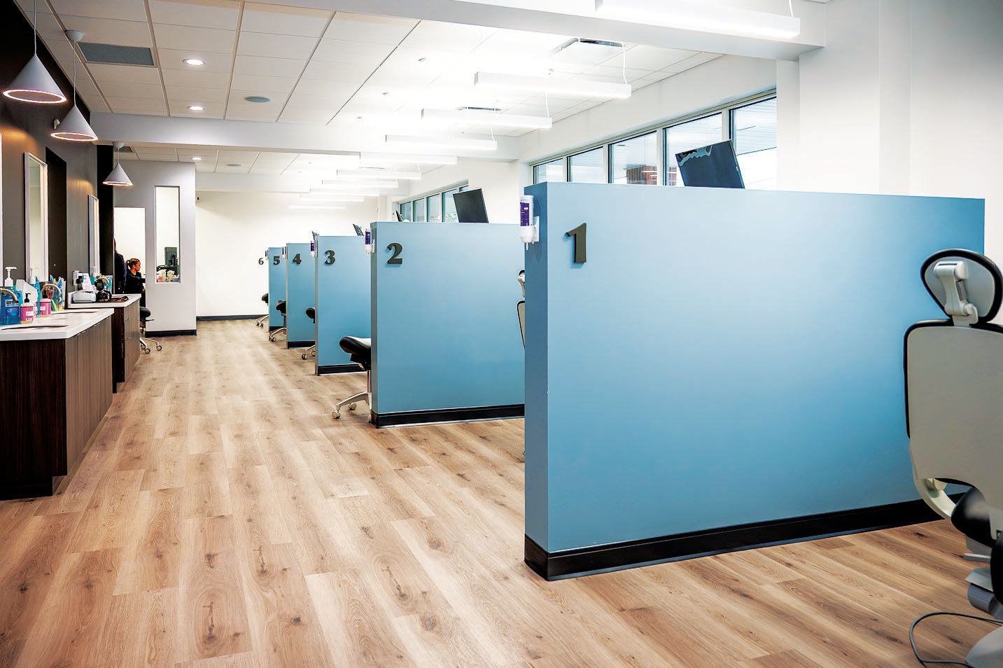A row of numbered blue partitions creating private service stations in a brightly lit, modern medical or salon office.